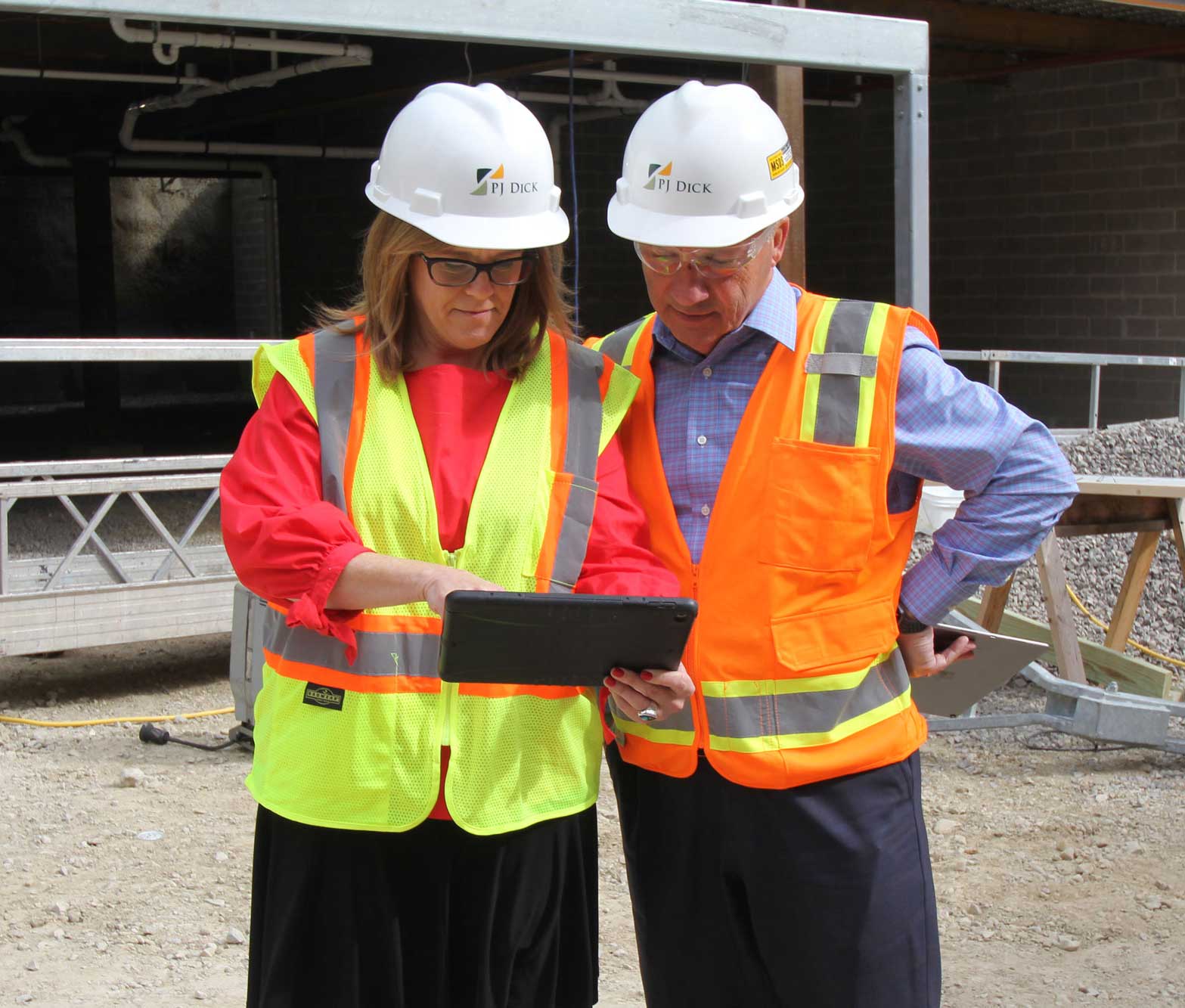 Two PJ Dick employees wearing safety gear looking at ipad