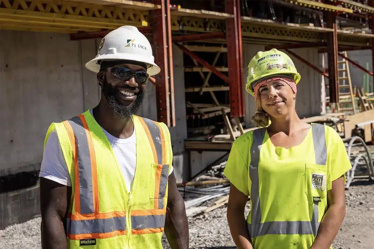 Man and woman smiling in construction vests and hard hats